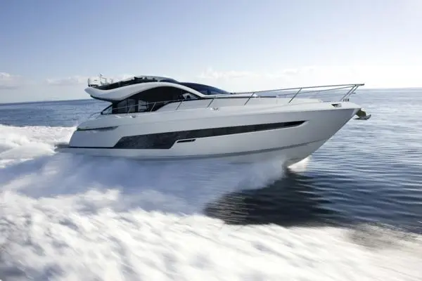 A sleek white motor yacht glides through calm waters, leaving a frothy wake against a clear blue sky.